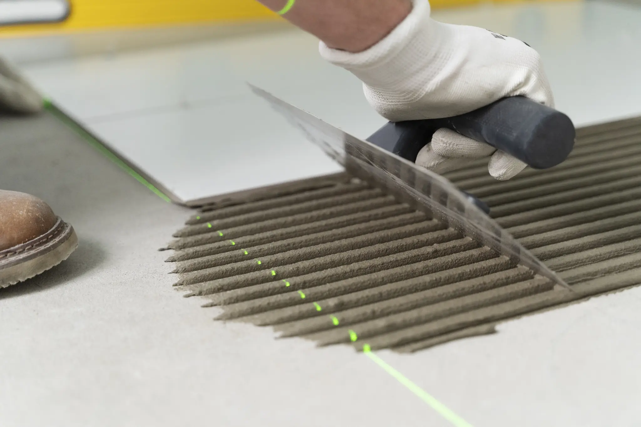 Fliesenleger trägt Fliesenkleber mit der Zahnkelle auf